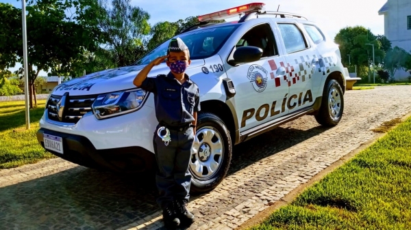O pequeno Enzo, fardado, ao lado da viatura da PM, em Mariápolis (Divulgação/PM).