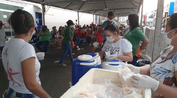 Pessoal que espera na fila, sentado e protegido com a tenda, recebe café da manhã (Da Assessoria).