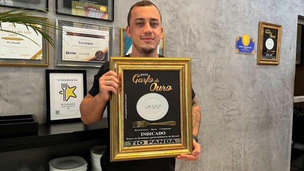 Diante da galeria com premiações, o empresário Vinícius Nogueira e a nova placa Garfo de Ouro 2022 (Foto: Siga Mais).