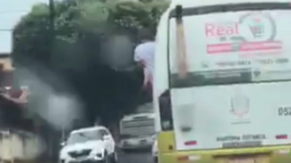 Passageiro escolar com parte do corpo para fora do ônibus, em flagrante de vídeo feito por morador (Reprodução).