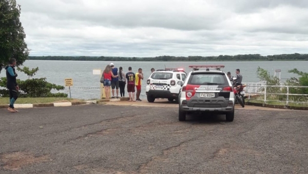 Equipes policiais e populares no local onde foi feita a retirada do corpo das águas do Rio Paraná (Reprodução/G1).